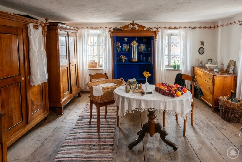 Schöne Stube Stilvoll eingerichtetes Esszimmer mit antiken Möbeln, zwei Fenstern, einem runden Tisch und einem großen blauen Schrank.