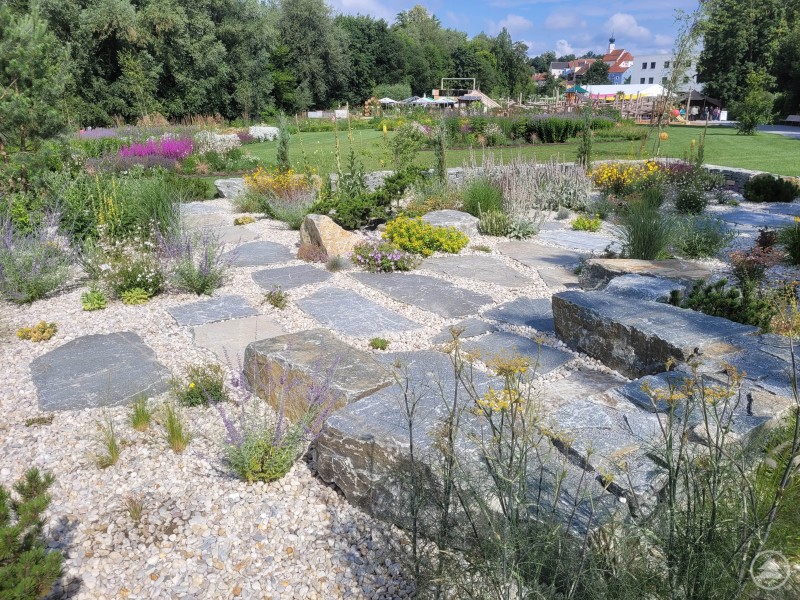 Die Themengärten sollen auch nach der Schau ein Ort der Begegnung und des Gestaltens bleiben. Ein Steingarten mit flachen Steinplatten, Kies und blühenden Stauden liegt eingebettet in eine weitläufige Grünanlage mit Blick auf Schärding.