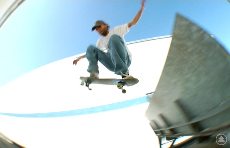 Skater der Crew „HELLABLAZER94“ beim Sprung – Szene aus dem neuen Skatevideo, das im Zeughaus Premiere feiert. Unscharfes Action-Foto eines Skateboarders in Jeans, T-Shirt und Basecap, der mit seinem Skateboard einen Sprung über eine Rampe bei blauem Himmel macht. Die Dynamik und Geschwindigkeit sind spürbar.