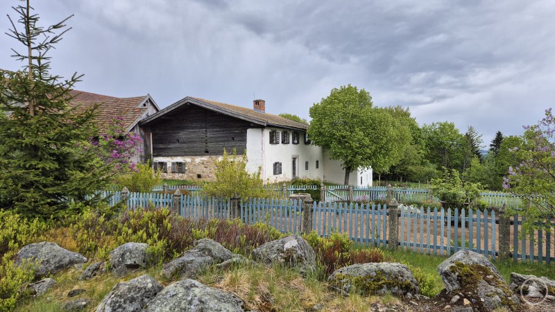 Der Garten vor dem Petzi Hof Außenaufnahme eines historischen Bauernhauses mit Holzbalkon, umgeben von einem Garten und einem Holzzaun.