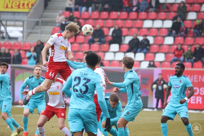 Intensive Zweikämpfe im Strafraum prägten das Duell zwischen dem SSV Jahn Regensburg und Viktoria Köln. Mehrere Spieler des SSV Jahn Regensburg und von Viktoria Köln steigen im Strafraum zum Kopfball hoch. Ein Jahn-Spieler setzt sich im Luftduell gegen mehrere Gegenspieler durch, im Hintergrund sind die roten Sitzreihen des Jahnstadions zu sehen.