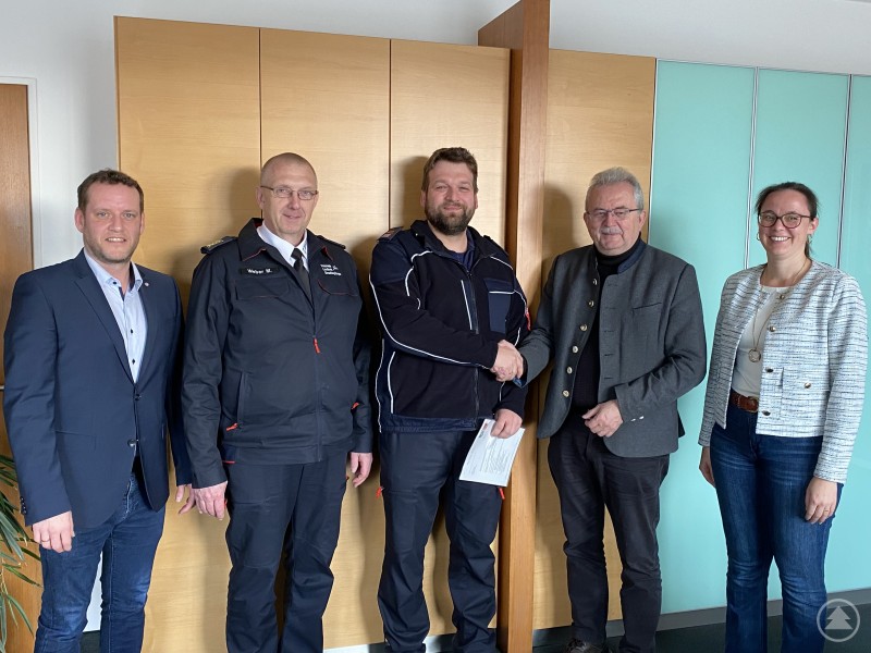 Jürgen Biermeier (Sachbearbeiter Feuerwehrwesen), Kreisbrandrat Markus Weber, der neue Fachberater Drohne, Franz Sträußl, Landrat Josef Laumer und die zuständige Abteilungsleiterin Stephanie Aumer (von links) bei der Aushändigung der Bestellung im Büro des Landrats. Fünf Personen stehen in einem Büro vor hellen Holzschränken und einer türkisfarbenen Wand. In der Mitte überreicht Landrat Josef Laumer dem neuen Fachberater Feuerwehrdrohne Franz Sträußl ein Dokument.