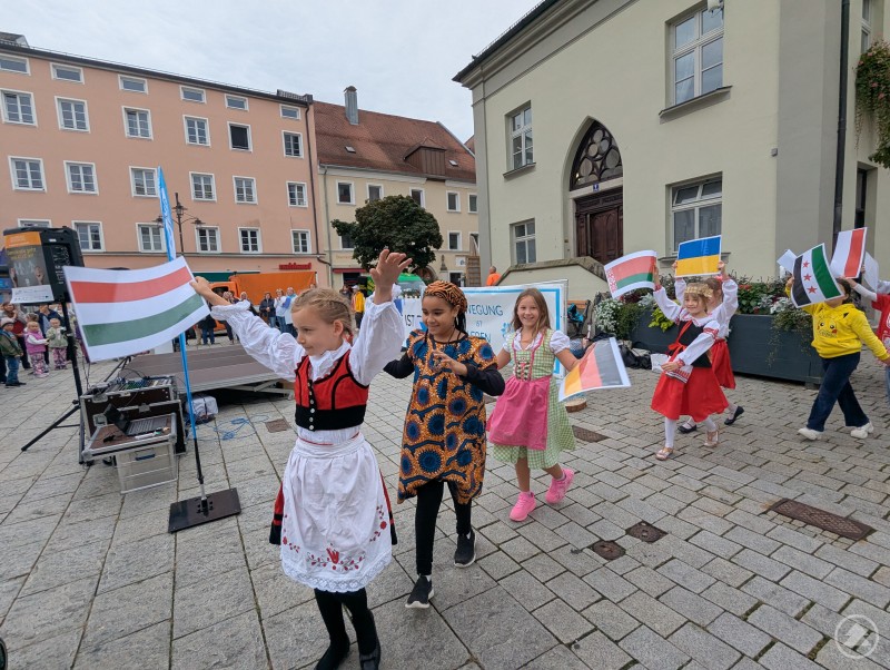 Vor dem Tanz-Flashmob zeigten Kinder, wie unterschiedlich traditionelle Mode in verschiedenen Ländern ist. Kinder in internationaler Tracht halten Fahnen verschiedener Länder in die Luft