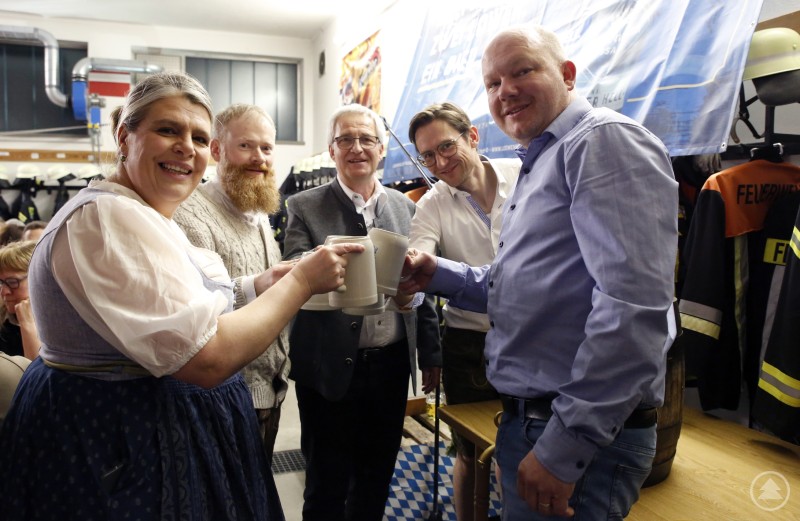 Die Röcklin, der Markus, der dorfeigene Biergermeister Max Riedl, der zweite Feuerwehrvereinsvorstand Schreiner Manuel und Alexander Ritzinger als Löwenbocklieferant stießen auf ein zünftiges Abwatschen an. Mehrere Personen stehen in einem Feuerwehrraum zusammen, stoßen mit Maßkrügen an und lächeln in die Kamera. Im Hintergrund sind Feuerwehruniformen und Ausrüstung zu sehen.