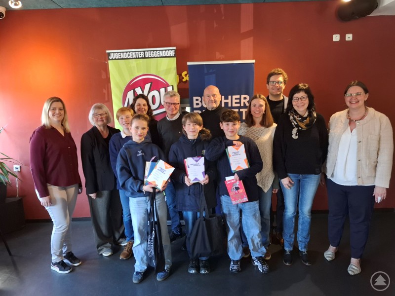 Das Siegerfoto in der Mitte mit der Urkunde Leitl Maximilian als Sieger, links davon die zweitplatzierte Karolin Niedermayer und rechts der drittplatzierte Luca Sichhart. Mit auf dem Foto die Jury und die Ehrengäste Stadtrat und Kreisjugendbeauftragter Paul Linsmaier, Landrat Bernd Sibler und Jugendbeauftragter Konrad Rankl Eine Gruppe aus Kindern und Erwachsenen steht im Jugendcenter 4You für ein Siegerfoto zusammen. In der Mitte halten die ausgezeichneten Teilnehmenden ihre Urkunden und Buchgeschenke in den Händen.