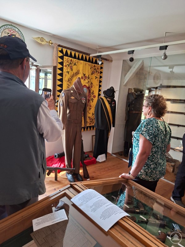 Besuchergruppe betrachtet eine US-Soldatenuniform und historische Exponate in einem Museumsraum. Uniform von Robert Patton als Ausstellungsstück im Stadtmuseum Schärding, bestaunt von seinen Nachkommen.