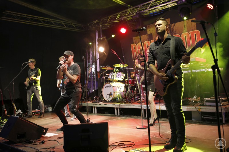 Rockband mit fünf Mitgliedern auf großer Bühne, intensives Bühnenlicht, energiegeladene Performance.