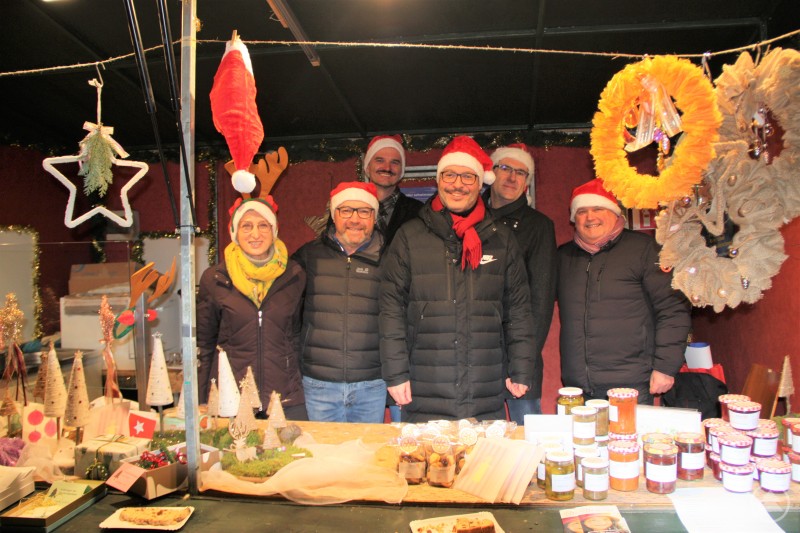 Das Team des Rotary-Clubs Passau-Dreiflüssestadt engagierte sich auf dem Christkindlmarkt mit einer Spendenaktion für bedürftige Kinder. Sechs Menschen stehen fröhlich nebeneinander in einer festlich geschmückten Marktbude. Sie tragen alle Weihnachtsmützen und warme Winterjacken. Vor ihnen sind weihnachtliche Dekoartikel und viele Gläser mit selbstgemachten Köstlichkeiten aufgebaut.