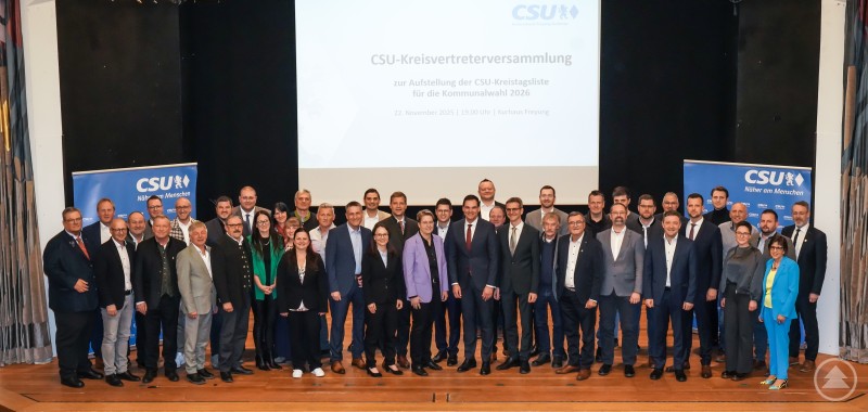 Die CSU Freyung-Grafenau hat ihre Liste für die Kreistagswahl 2026 aufgestellt: Die Kandidatinnen und Kandidaten um Landrat Sebastian Gruber und CSU-Kreisvorsitzenden Dr. Olaf Heinrich. Eine große Gruppe von Männern und Frauen steht auf einer Bühne vor einer Leinwand, auf der die CSU-Kreisvertreterversammlung zur Aufstellung der Kreistagsliste für die Kommunalwahl 2026 angekündigt wird. Im Hintergrund stehen zwei CSU-Banner, die Teilnehmenden tragen überwiegend festliche oder geschäftliche Kleidung.