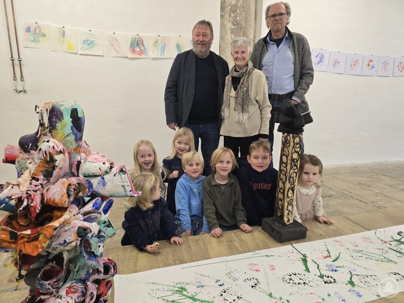 Sie begeisterten die Kinder mit ihrer Leidenschaft für Kunst. V.li.: Hubert Huber Waltraud Danzig und Ernst Zahnweh. Mehrere Kindergartenkinder sitzen vor einem großen Papier am Boden, dahinter stehen drei Erwachsene neben einem Kunstobjekt, im Hintergrund hängen Kinderbilder an der Wand.