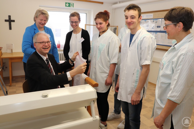 Domkapitular Josef Ederer legt an der Bügelmaschine vor. Die namensgleiche Kreisrätin Annemarie Ederer (v.li.) und Dr. Martina Hartl packen anschließend an. Vanessa Neustifter und Jonas Klein mit ihrer Teamleiterin Marianne Trauner haben die Arbeit erklärt.