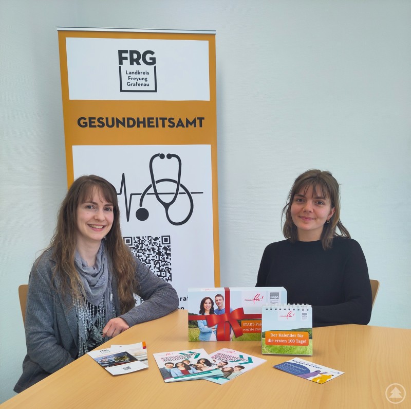 Amtsärztin Dr. med. Karin Drachsler (links) und Sozialpädagogin Sarah Knors (beide Gesundheitsamt Freyung-Grafenau) beantworten Fragen zum Thema Rauchen und informieren über Prävention und Hilfsangebote. Zwei Frauen sitzen an einem Tisch im Gesundheitsamt Freyung-Grafenau vor einem Aufsteller mit Logo und Info-Materialien zu Nichtraucherkampagnen.