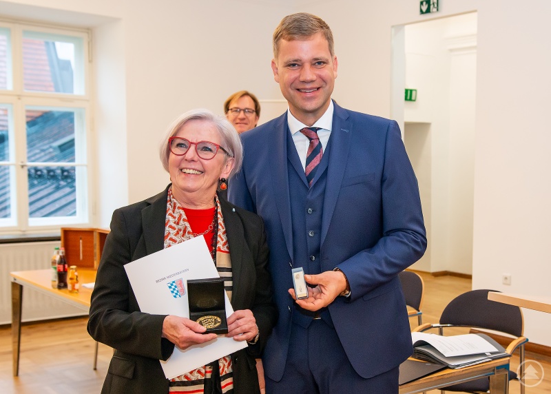 Bezirkstagspräsident Dr. Olaf Heinrich überreicht der ehemaligen Bezirksrätin und weiteren Stellvertreterin des Bezirkstagspräsidenten die Große Goldene Bezirksmedaille.