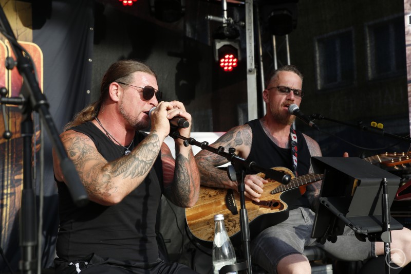 Zwei Musiker mit Gitarren und Tattoos sitzen auf der Bühne und performen unplugged.