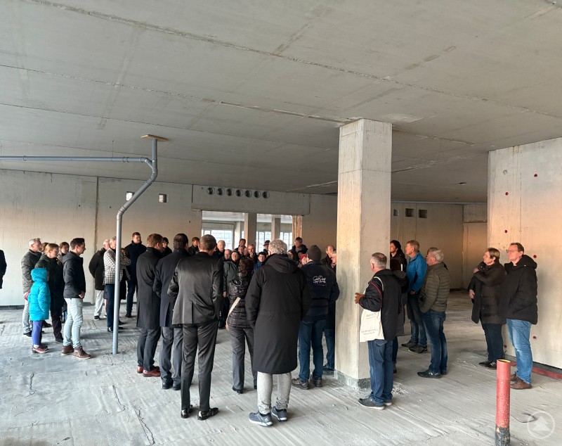 Reges Interesse bei der Baustellenbesichtigung des Fördervereins am Krankenhaus Freyung. Eine größere Gruppe von Menschen, teils in Anzügen, teils in Freizeitkleidung, steht in einem Rohbau mit Betonboden und Betonstützen. Die Gruppe hört einer Führungsperson aufmerksam zu – es herrscht reges Interesse an der Baustelle.