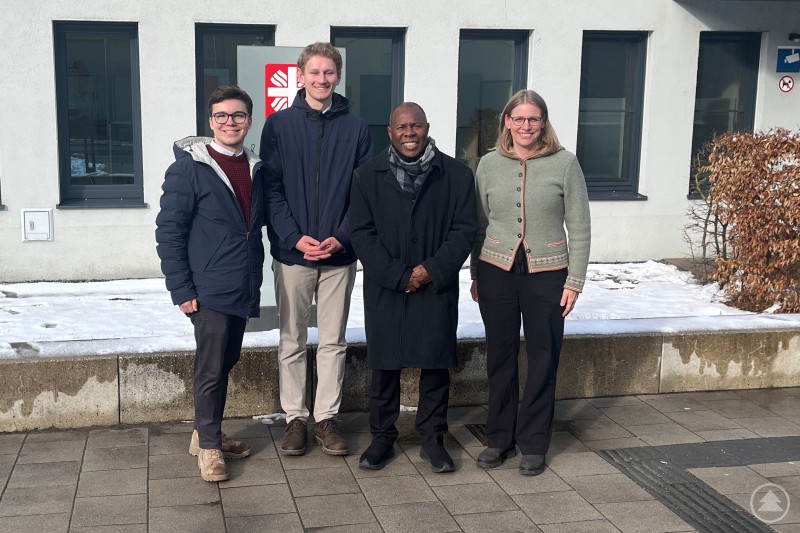 V.li. Niklas Klingel RCDS München, Maximilian Becker RCDS Passau, Weihbischof Vincent Frederick Mwakhwawa Erzbistum Lilongwe Malawi und Agnes Stefenelli Caritas beim Besuch im Konradinum in Passau. Vier Personen stehen vor dem Gebäude des Konradinums in Passau und posieren für ein Gruppenfoto im Freien.