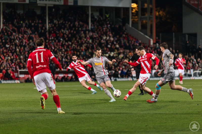 Mehrere Spieler des SSV Jahn Regensburg und des FC Energie Cottbus k&auml;mpfen in einer Spielsituation um den Ball im Strafraum. Die Kulisse ist das vollbesetzte Stadion bei Flutlicht.