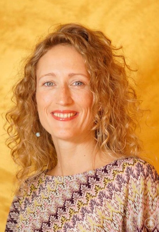 Protrait von Marlene Egger mit warmen farben im Hintergrund. Sie hat lockiges blondes Haar und blaue Augen und l&auml;chelt herzlich.