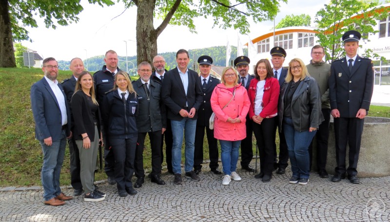 Landrat Sebastian Gruber (Mitte) mit Führungskräften der Kreisbrandinspektion, Mitarbeitenden des Landratsamtes und Feuerwehrvertretern aus der Partnerstadt Třeboň beim grenzüberschreitenden Austausch. Eine Gruppe von etwa 17 Personen steht auf einem gepflasterten Platz unter Bäumen. Einige der Personen tragen Feuerwehruniformen, andere sind in zivil gekleidet. Im Hintergrund ist das Gebäude des Landratsamts Freyung-Grafenau zu sehen.