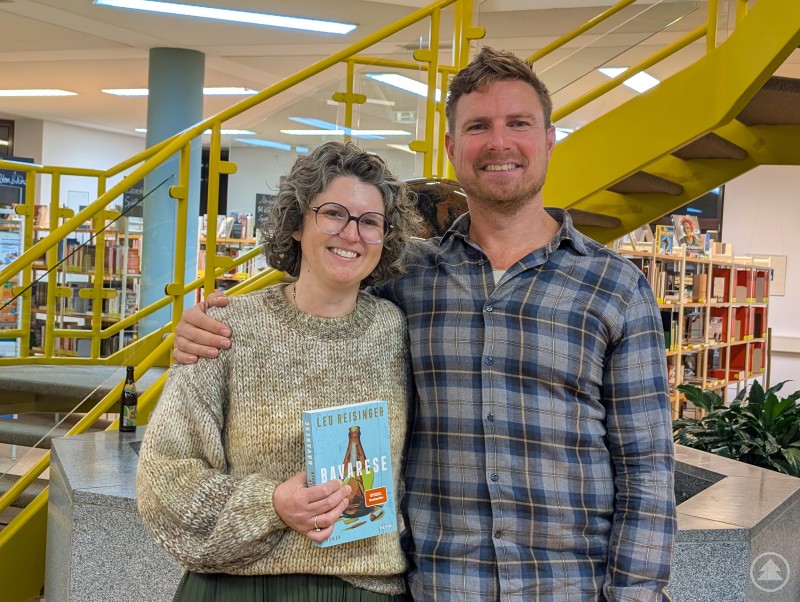 Michaela Benzinger, Leiterin der Kreisbibliothek Freyung-Grafenau, mit Schauspieler und Autor Leo Reisinger nach der gelungenen Lesung. Leo Reisinger steht neben Michaela Benzinger, der Leiterin der Kreisbibliothek Freyung-Grafenau. Beide lächeln in die Kamera, im Hintergrund sind Bücherregale zu sehen.
