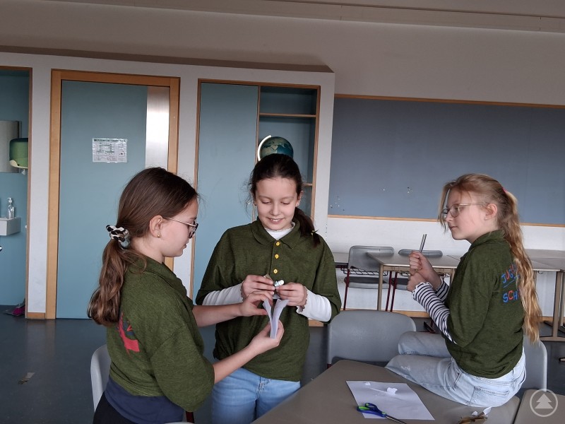 Drei Jugendliche sitzen an einem Tisch und basteln gemeinsam, konzentriert bei einer kreativen Aufgabe.