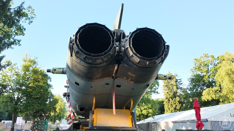 Rückansicht eines Tornado-Kampfjets. Die beiden Triebwerksdüsen dominieren das Bild, darunter ein gelber Rollwagen. Im Hintergrund Bäume und Zelte.