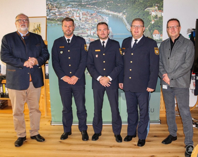 Oberbürgermeister Jürgen Dupper (links) beim Antrittsbesuch zusammen mit (v. l.) Polizeioberrat Sebastian Feucht, Polizeirat Moritz Lehner, Polizeidirektor Christian Dichtl und dem Leiter des Ordnungsamtes Erik Linseisen. Fünf Männer stehen nebeneinander in einem Büro vor einem großen Wandbild von Passau. Drei von ihnen tragen dunkelblaue Polizeiuniformen, die beiden anderen sind zivil gekleidet.