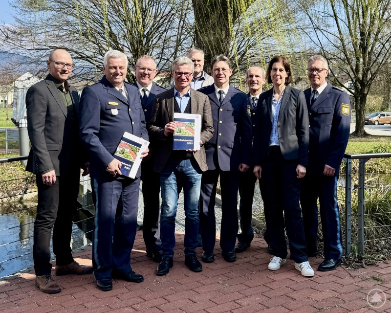 Von links: Erster Kriminalhauptkommissar Andreas Polke, Polizeivizepräsident Werner Sika, Polizeidirektor Markus Völkl, Landrat Bernd Sibler, Thomas Kindel, Polizeipräsident Roland Kerscher, Erster Polizeihauptkommissar Elmar Kastl, Leitende Kriminaldirektorin Annette Haberl, Erster Polizeihauptkommissar Frank Schlenz Neun Personen aus Polizei und Landratsamt stehen für ein Gruppenfoto im Freien an einem Geländer vor einem kleinen Gewässer.