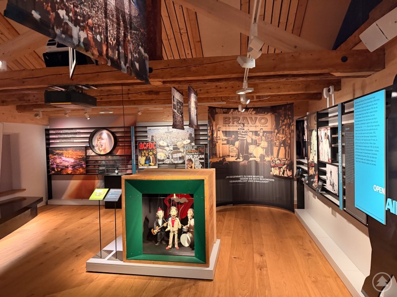Einblick in die vielfältige Musikgeschichte Bayerns mit Exponaten von Rock bis Pop. Ein liebevoll gestalteter Ausstellungsraum mit historischen Musikmotiven, Plattencovern, Fotos und einer Vitrine mit Figuren.