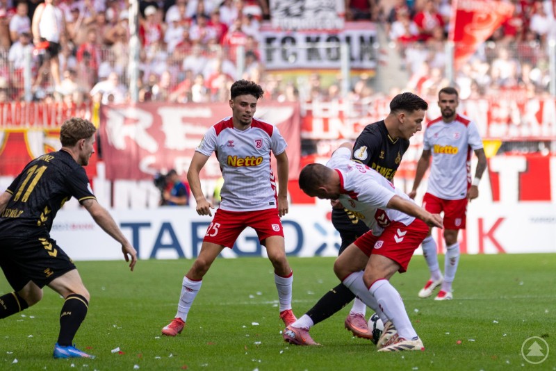 Zwei Spieler des SSV Jahn im Zweikampf mit Kölner Gegenspielern im Mittelfeld.