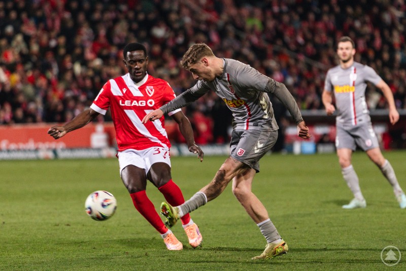 Immer gefährlich: Die Jahnelf suchte immer wieder den Weg zum Tor des FC Energie Cottbus. Ein Jahn-Spieler schießt den Ball, während ein Cottbuser Gegenspieler versucht zu blocken. Im Hintergrund beobachten weitere Spieler die Szene.