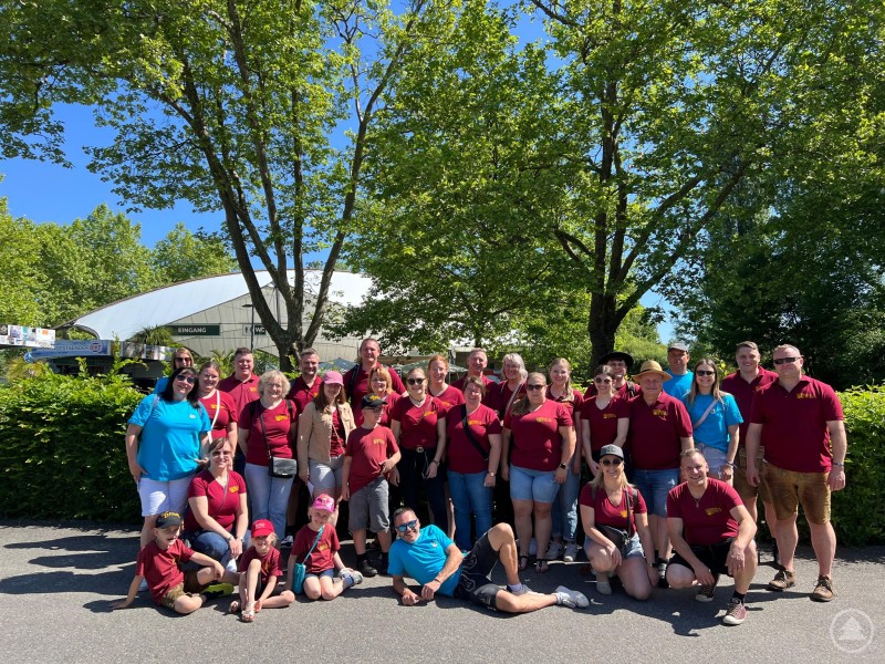 Gruppenbild von etwa 30 Personen in roten Vereins-T-Shirts vor dem Eingang zur Insel Mainau bei sonnigem Wetter.