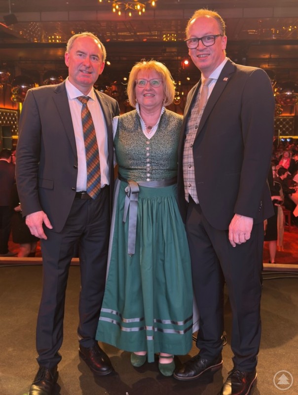 Bürgermeisterkandidatin Monika Beham beim Neujahrsempfang der FREIE WÄHLER Landtagsfraktion auf dem Münchner Nockherberg. Zwei Männer im Anzug und eine Frau im festlichen Dirndl stehen eng beieinander auf einer Bühne. Im Hintergrund ist ein festlich beleuchteter Saal mit Gästen zu sehen.