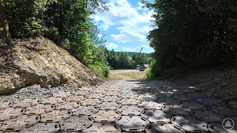 Ein steiler Zufahrtsweg, mit massiven Panzerplatten ausgelegt, führt hinunter ins Gelände. Im Hintergrund sind Fahrzeuge und ein Kran erkennbar.