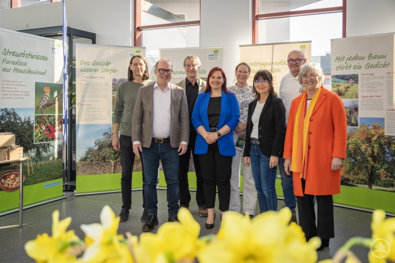 Foto v.l.n.r.: Georg Kestel-Kreisvorsitzender BUND Naturschutz Deggendorf, Christoph Strasser-Leiter Bauamt Stadt Deggendorf, Klaus Busch-Sachgebietsleiter Stadtplanungsamt, Sabrina Diyaroglu-Leiterin Geschäftsstelle Streuobstwiesenkompetenzzentrum Lalling, Stefanie Arneth-Stadtplanungsamt, Claudia Brielbeck-Schulamtsdirektorin Staatliches Schulamt Deggendorf, Robert Schneider-Leiter Stadtgärtnerei, Maria Gruber, Vorstandsvorsitzende des Niederbayerischen Streuobstwiesenkompetenzzentrums Lallinger Winkel e.V. Eine Gruppe von acht Personen steht im Rathaus vor mehreren Ausstellungstafeln zum Thema Streuobstwiesen. Im Vordergrund sind gelbe Blumen unscharf zu sehen.