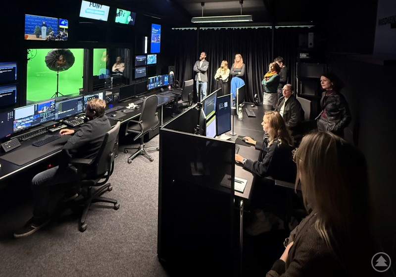 Austausch der Donaustädte Regensburg, Straubing, Deggendorf und Passau im Medienatelier der Stadt Deggendorf Mehrere Personen verfolgen in einem modernen Medienraum Bildschirme und Produktionen an Arbeitsplätzen