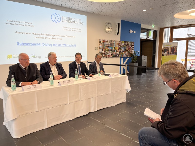 Im Anschluss an die Landrätetagung standen Landrat Franz Löffler, Landrat Richard Reisinger, Landrat Sebastian Gruber und Landkreistagspräsident Thomas Karmasin (von links) den Pressevertretern Rede und Antwort. Vier Landräte sitzen an einem weiß gedeckten Tisch mit Mikrofonen und Wasserflaschen, während ein Journalist Fragen stellt. Im Hintergrund eine Wand mit Logos und dem Schriftzug „Dialog mit der Wirtschaft“.
