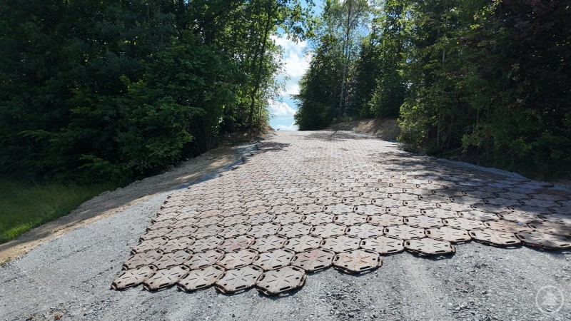 Panzerplatten bedecken eine breite Zufahrt durch einen bewaldeten Einschnitt. Die Platten liegen dicht und bilden eine stabile Fahrbahn.