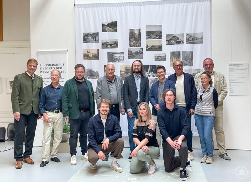 Bezirkstagspräsident Dr. Olaf Heinrich (hinten v. l.) mit dem ehem. Leiter der Landesstelle für nichtstaatliche Museen, Georg Waldemer, Bürgermeister Heiner Kilger, Josef Auer, Gregor Salatmeier, Dr. Patrick Reitinger, stv. Landrat Franz Brunner, Prof. Dr. Thomas Porada, Dr. Sandra Kreisslová sowie (vorne v. l.) die studentischen Hilfskräfte Jens Heinrich, Inga Förtsch und Maximilian Lenk. Gruppe von Wissenschaftlern und Museumsvertretern posiert vor einer Ausstellungstafel mit historischen Fotos im Freilichtmuseum Finsterau.