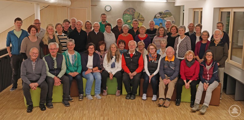 Waldführerinnen und Waldführer stellten sich am Ende noch zusammen mit dem Umweltbildungsteam des Nationalparks zum Gruppenfoto in der neu entstandenen Empore des Jugendwaldheim-Speisesaals auf. Eine große Gruppe von etwa 40 Personen, darunter Männer und Frauen unterschiedlichen Alters, steht und sitzt gemeinsam in einem hellen Raum auf einer Empore des Jugendwaldheims. Im Hintergrund sind Infotafeln und eine Uhr an der Wand zu sehen.