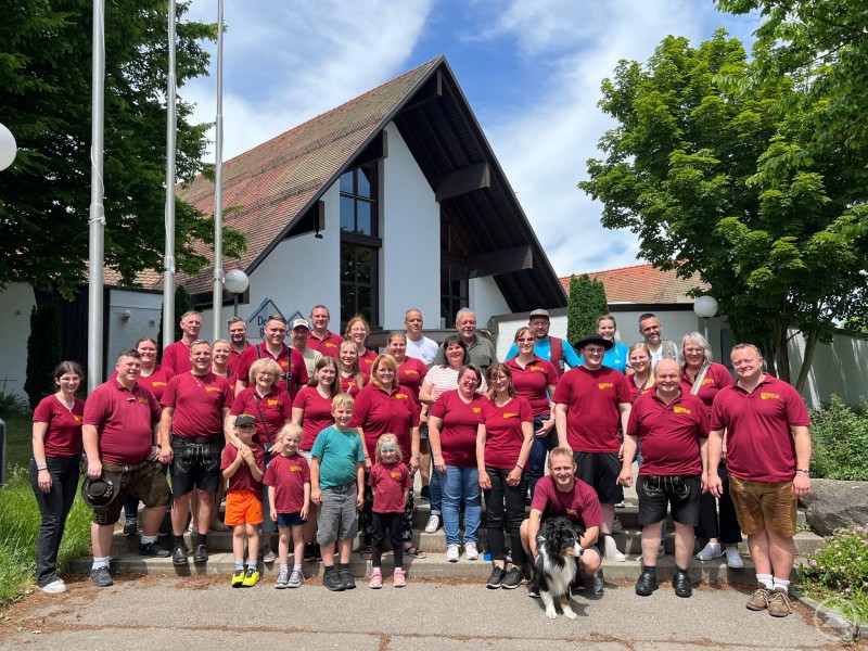 Gemeinschaftsfoto der Musikkapellen Schnetzenhausen und Haus i. Wald nach dem Empfang. Gruppenfoto aller Teilnehmer aus Haus i. Wald und Schnetzenhausen vor einem Gebäude bei sonnigem Wetter.