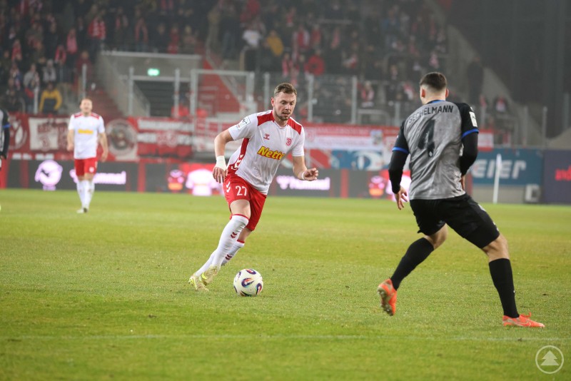 Der SSV Jahn Regensburg sucht mit Tempo den Weg nach vorne. Ein Jahn-Spieler im roten Trikot führt den Ball am Fuß und steuert auf einen Verteidiger des SV Waldhof Mannheim zu.