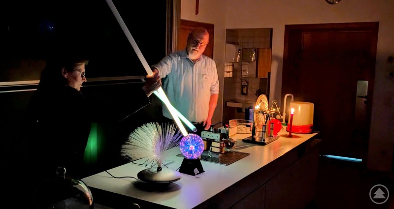 Im Fach Physik wurde mit Lichtschwertern und anderen technischen Highlights experimentiert. Ein Lehrer demonstriert in einem dunklen Physikraum ein leuchtendes Experiment mit Licht und technischen Geräten.