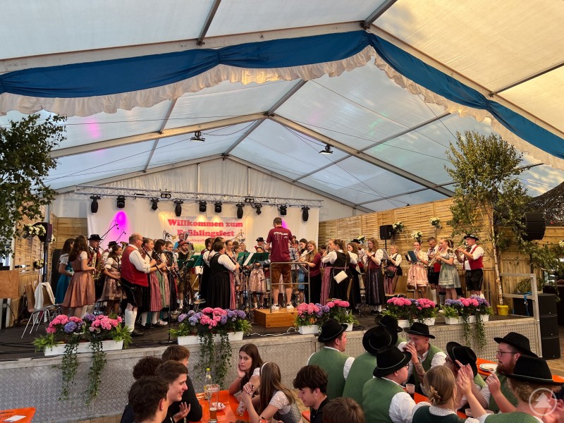 Blasmusiker mehrerer Kapellen spielen gemeinsam auf der Bühne eines Festzelts.