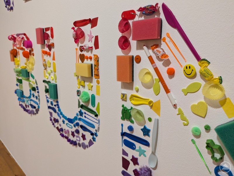 Kunterbunte Alltagsgegenstände, die einen Schriftzug bilden, begrüßen die Gäste zur Familien-Mitmach-Ausstellung. Bunte Alltagsgegenstände formen Schriftzug