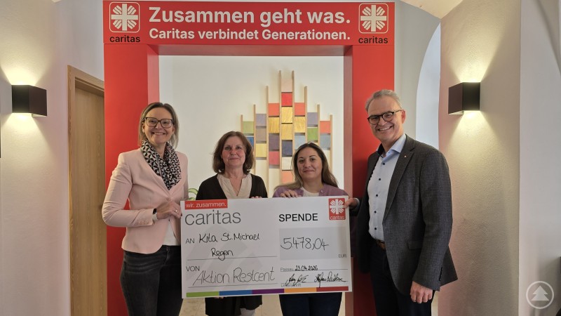 Förderung für die Zukunft der frühkindlichen Bildung: Der Kindergarten St. Michael in Regen erhält 5.478,04 Euro aus der Restcent-Aktion. Den Scheck nehmen Frau Dannerbauer aktuelle Leitung und Frau Reindl künftige Leitung entgegen, überreicht von Vorständin Andrea Anderlik und Vorstand Stefan Seiderer. Vier Personen stehen unter einem roten Caritas-Rahmen und präsentieren einen Spendenscheck für den Kindergarten St. Michael in Regen.