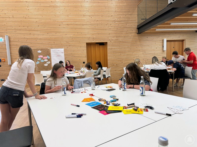 In Kleingruppen arbeiteten die Jugendlichen beim Jugendforum Zenting an ihren Ideen und Wünschen – kreativ, konzentriert und mit viel Engagement. Jugendliche sitzen an weißen Tischen und gestalten Plakate mit bunten Karten, Stiften und Materialien.