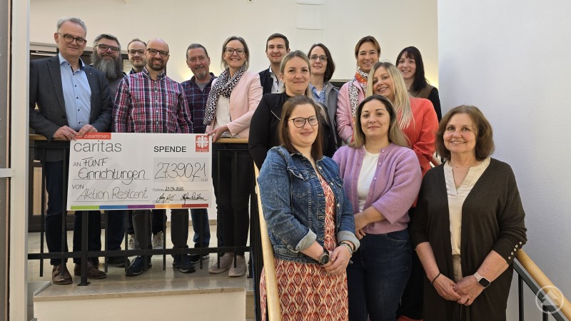 Gruppenfoto der Vertreterinnen und Vertreter mehrerer sozialer Einrichtungen bei der Scheck&uuml;bergabe der Caritas Restcent-Aktion in Passau. Gemeinsam pr&auml;sentieren sie einen symbolischen Spendenscheck &uuml;ber 27.390,21 Euro.