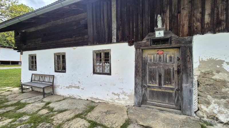 Sachl mit alter Tür und Bank vor dem Haus. Das Haus ist mit Holz verkleidet.