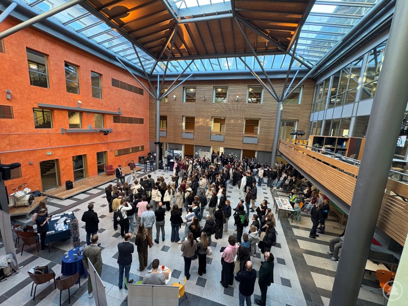 Viele Schülerinnen und Schüler versammeln sich in der Aula des Gymnasiums Freyung. Verschiedene Infostände, Hochschulvertreter und ein kleines Podest sind im modernen, lichtdurchfluteten Atrium zu sehen.